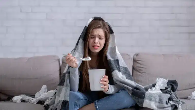 A woman eating ice cream, looking moody and tired, still craving more.